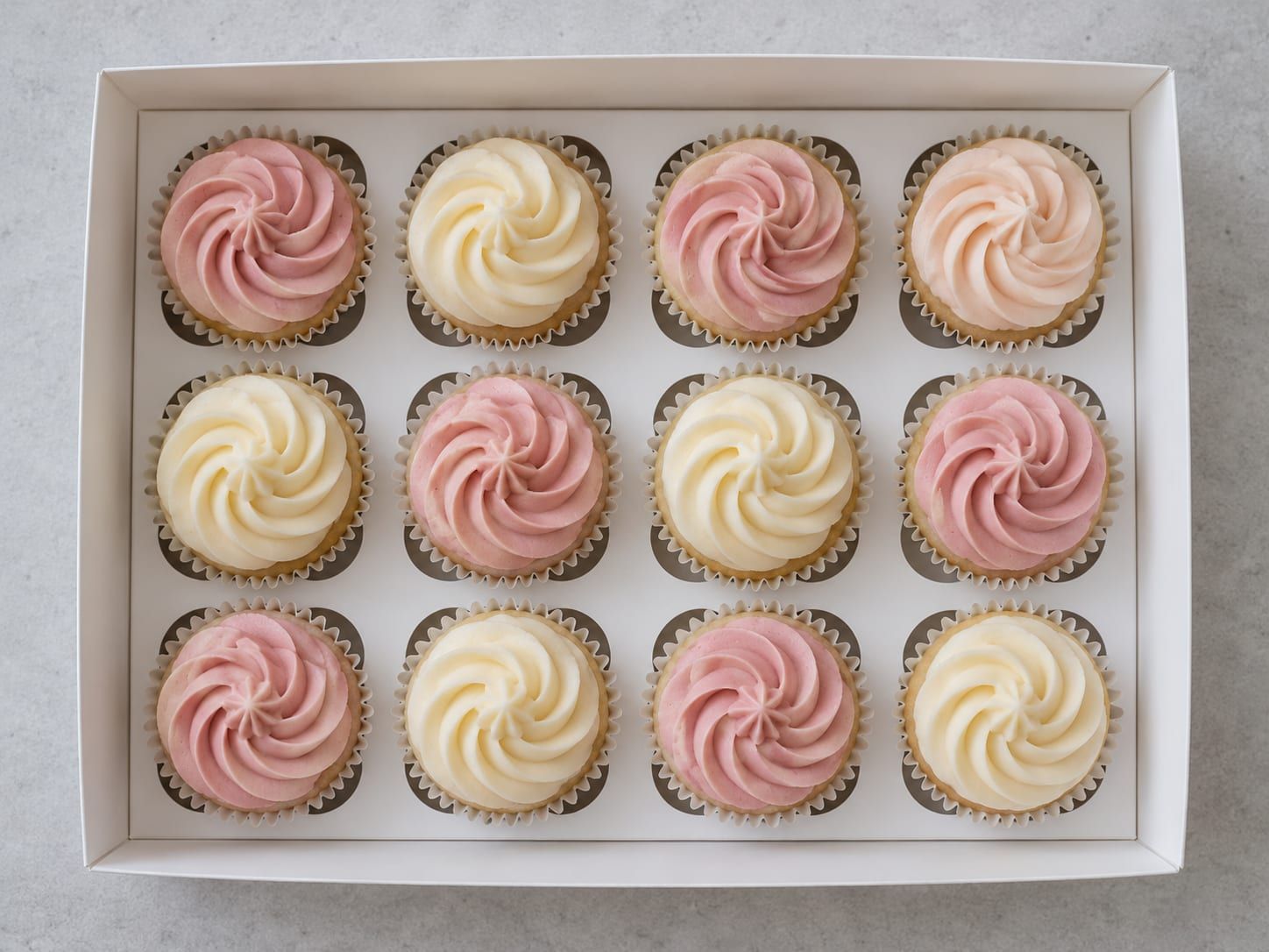 Twelve pastel buttercream cupcakes arranged in a box